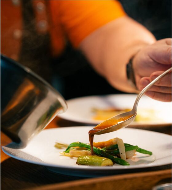 Le chef nappe de jus une assiette de légumes à la cuillère, cuisine de La Madeleine à Sens